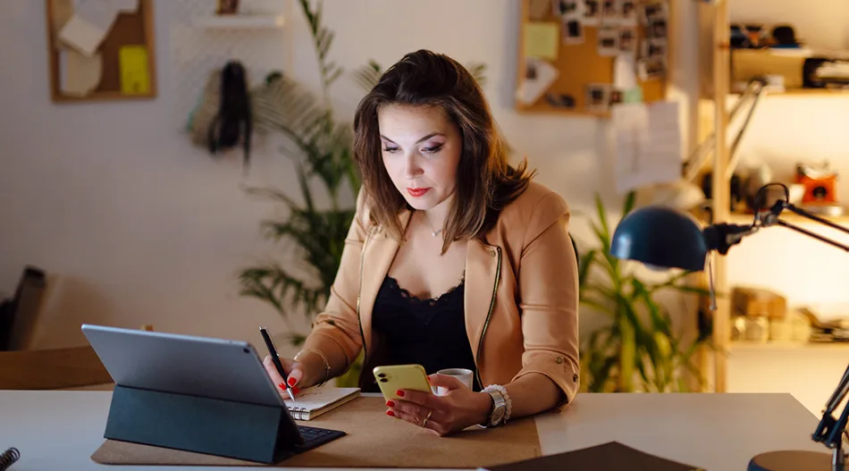 A woman in front of a laptop, looking at her phone